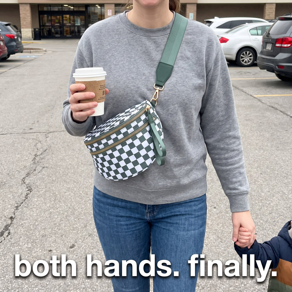 Mom wearing The Freehand crossbody bag with both hands free, holding coffee and her toddler's hand